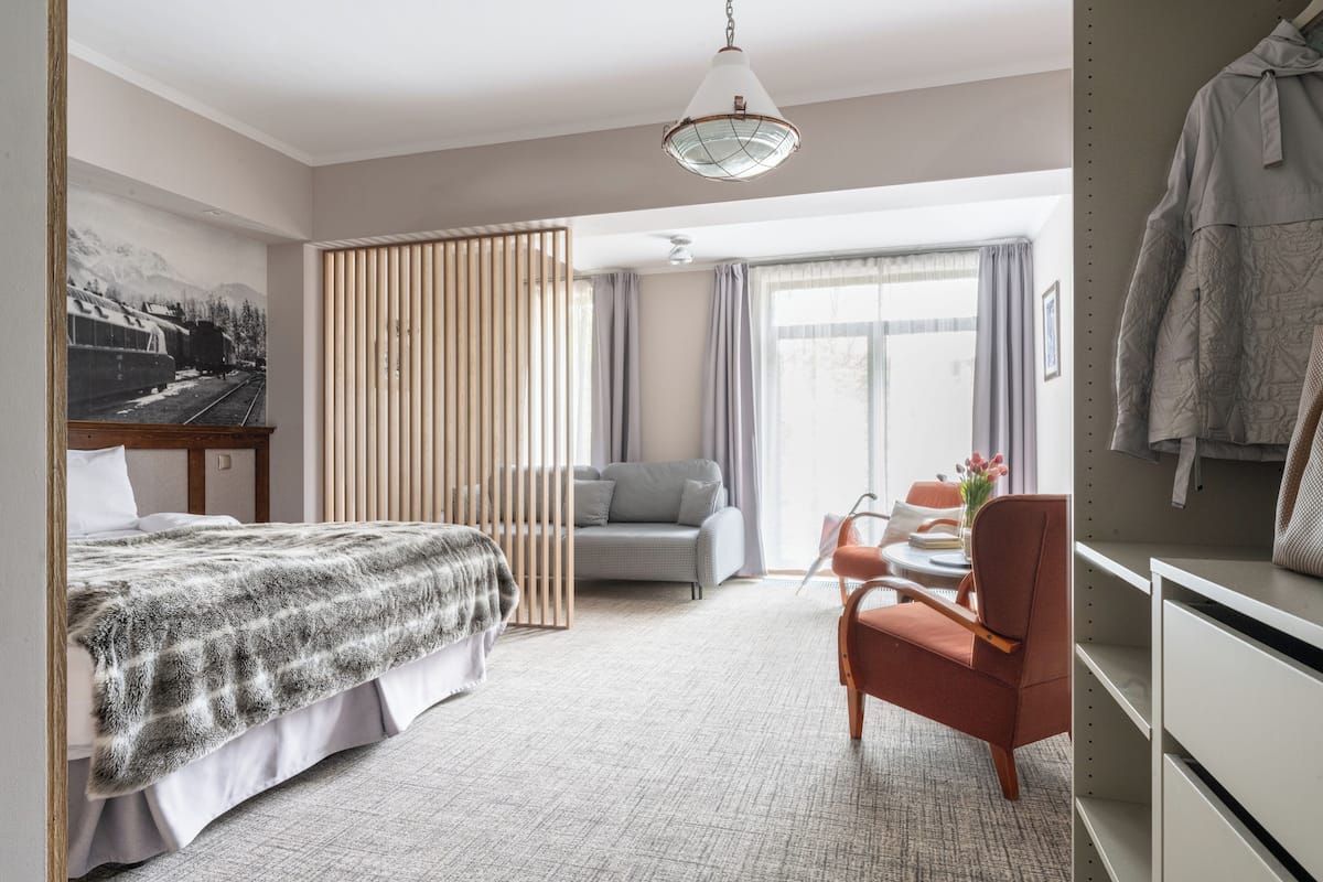 A hotel room with a bed, a sofa, a desk, and a chair. There is a window with curtains and a painting on the wall.