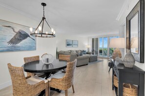 A modern living room with a dining area, featuring wicker furniture, a chandelier, and a view of the outdoors.