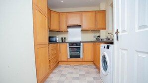 A compact kitchen with wooden cabinets, a built-in oven, a microwave, and a washing machine.