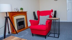 A living room with a red armchair, a small table, a fireplace, and a clock on the wall.