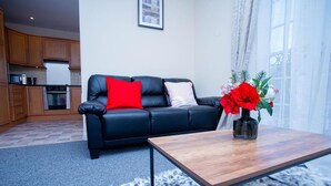 A living room with a black leather sofa, a wooden coffee table, and a vase with red flowers.