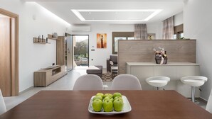 A modern dining area with a wooden table, white chairs, and a plate of green apples. - Panthea Villa in Ialysos (Ιαλυσός)