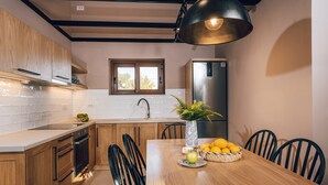 A modern kitchen with wooden cabinets, a stainless steel refrigerator, a dining table with chairs, and a vase with lemons and an apple. - Terra Lucis Mountain Residences/ Mare Villa (Zakynthos)