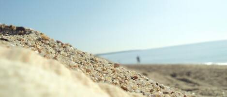 A close-up of a textured surface, likely a carpet or rug, with a blurred background featuring a person standing on a beach.