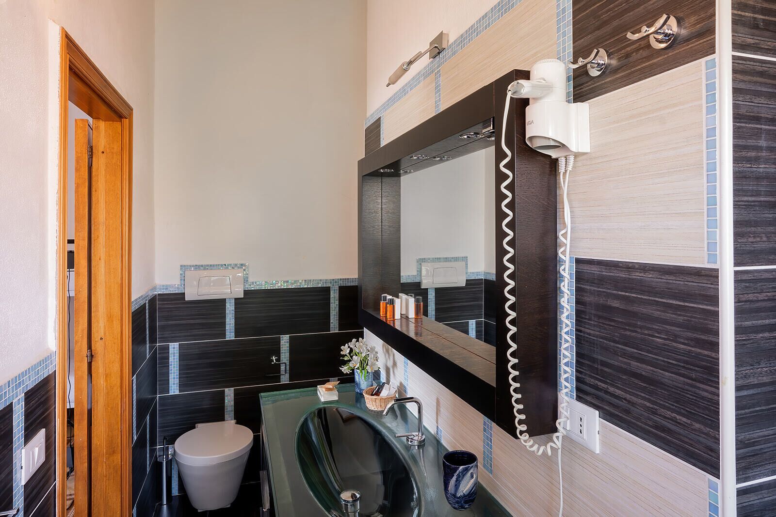 A compact bathroom with a glass sink, a toilet, and a hairdryer mounted on the wall.