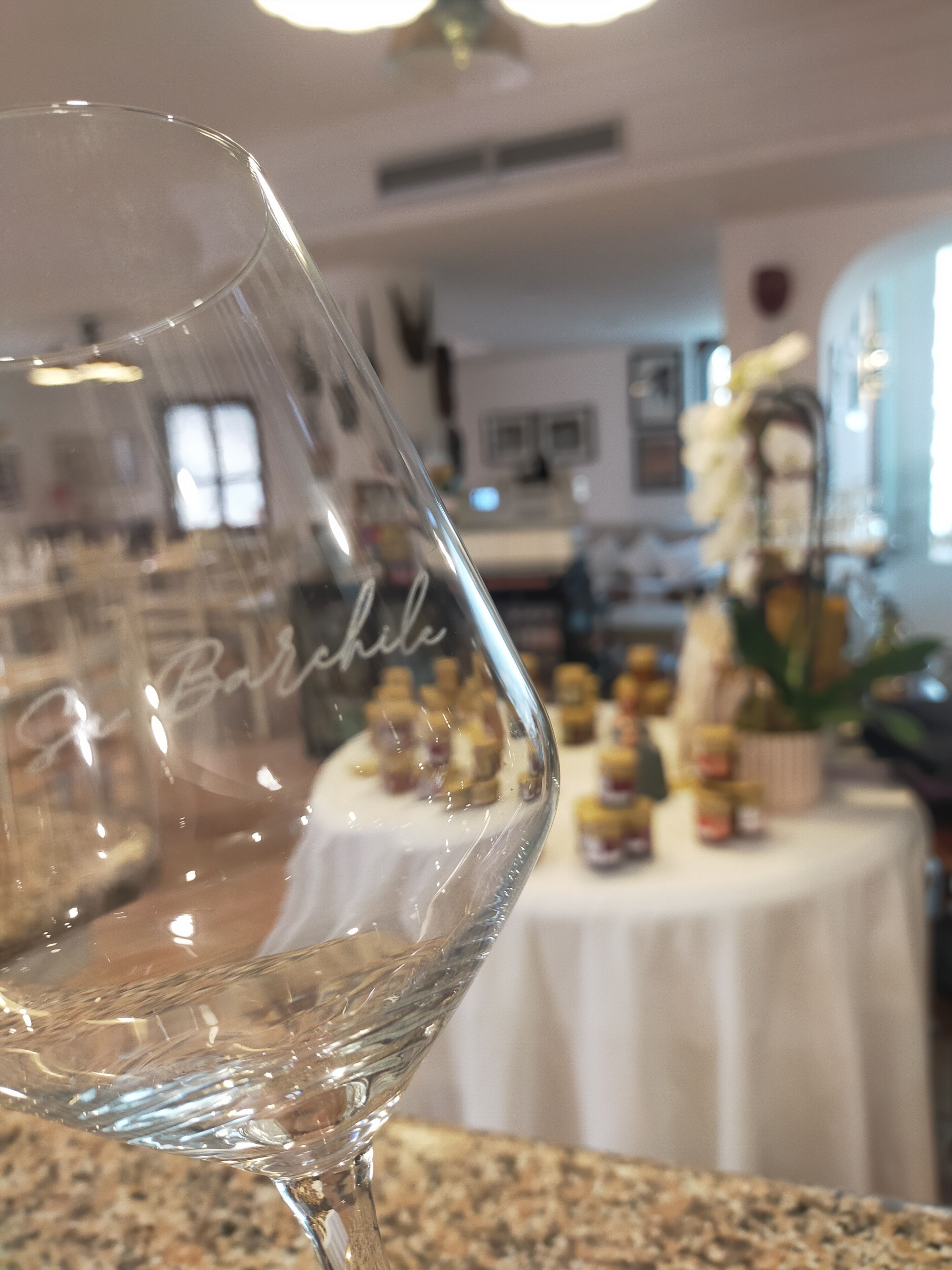 A clear glass with the inscription "Birch" on a table in a room with a white tablecloth, a window, and various items in the background.