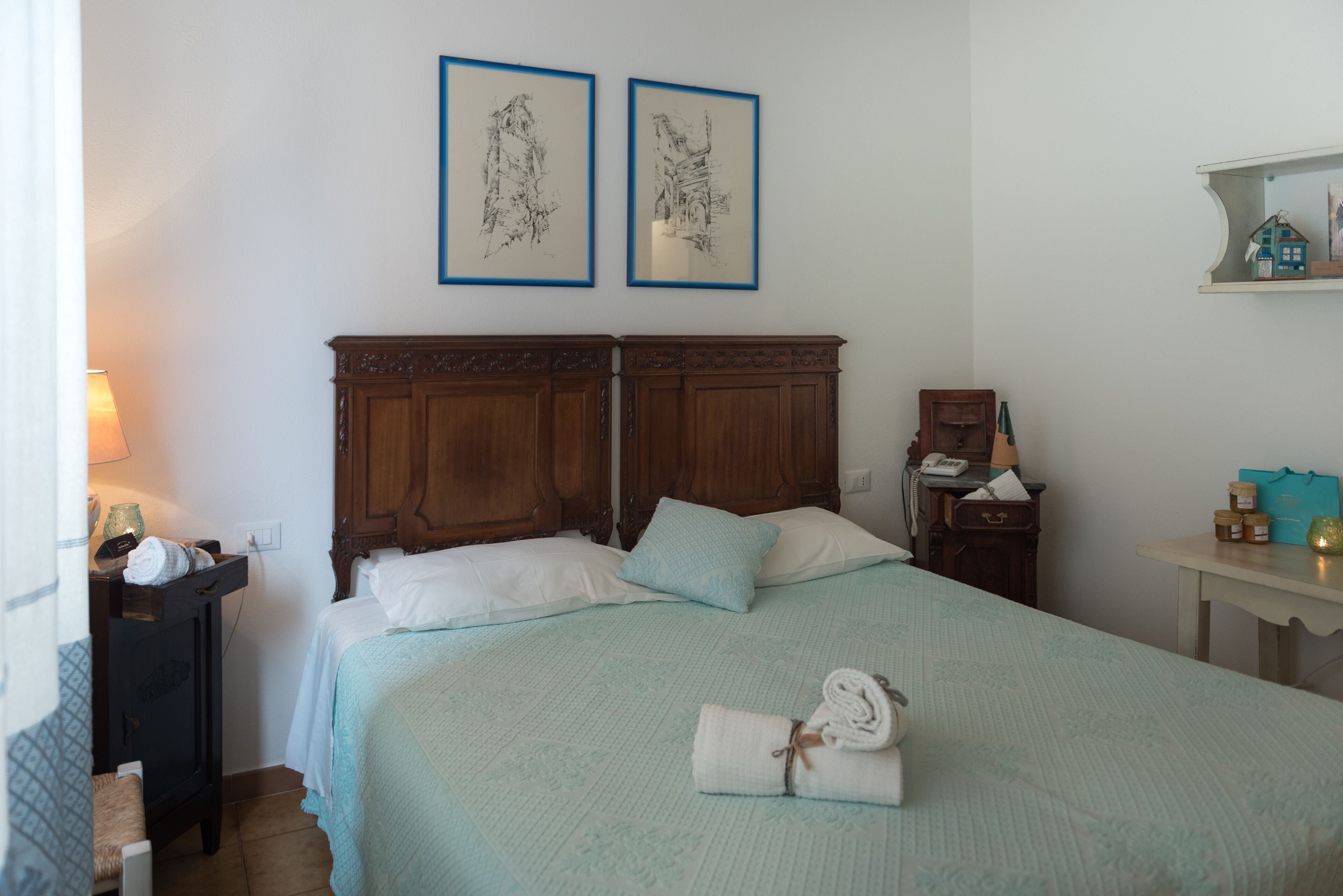 A hotel room with a large bed, a wooden headboard, a nightstand with a lamp, and two framed pictures on the wall.