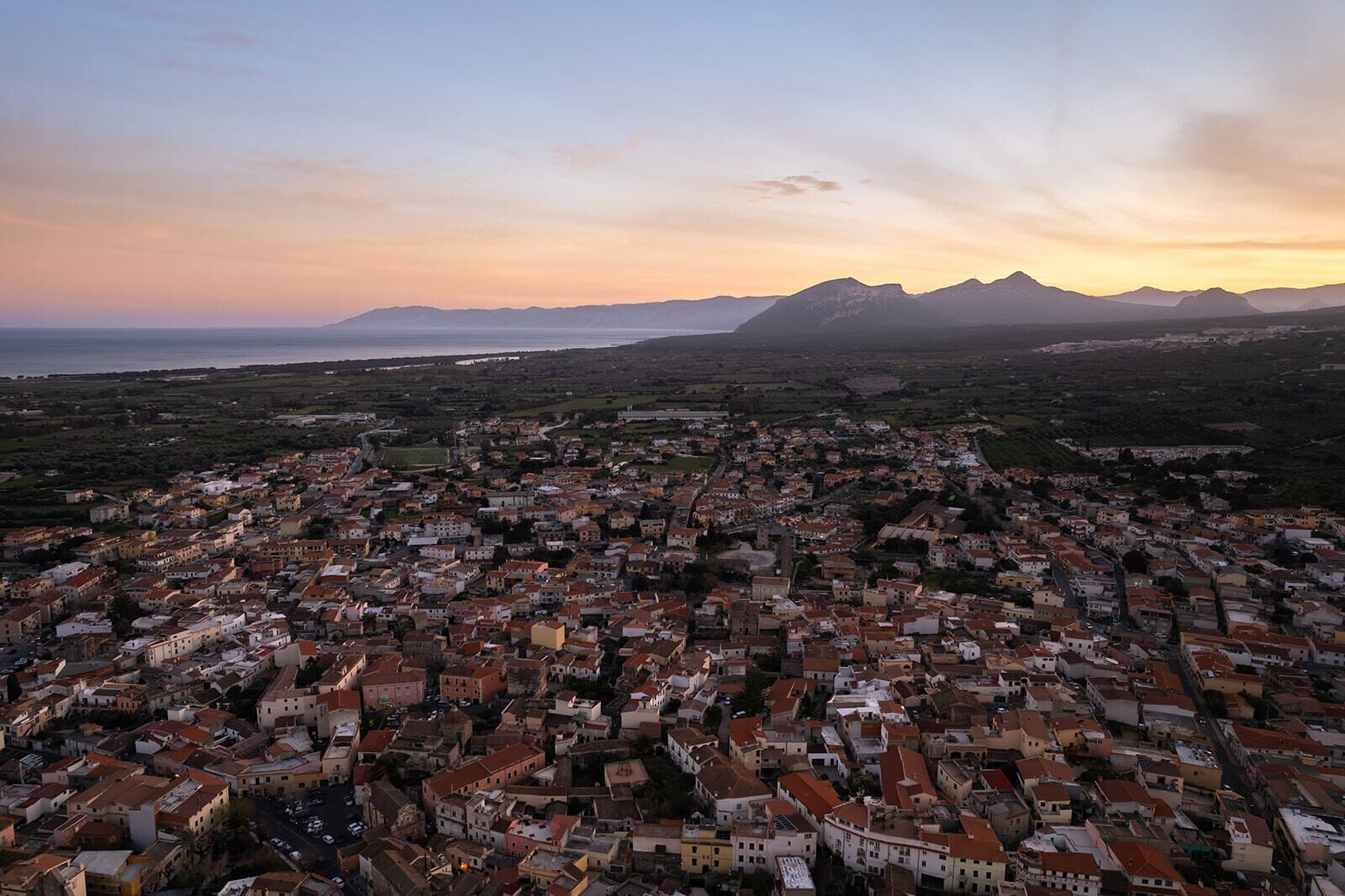 An aerial view of a coastal town with dense housing, a prominent church, and mountains in the background.