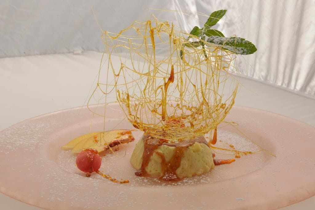 A dessert on a pink plate with a wire nest, a leaf, and a cherry.