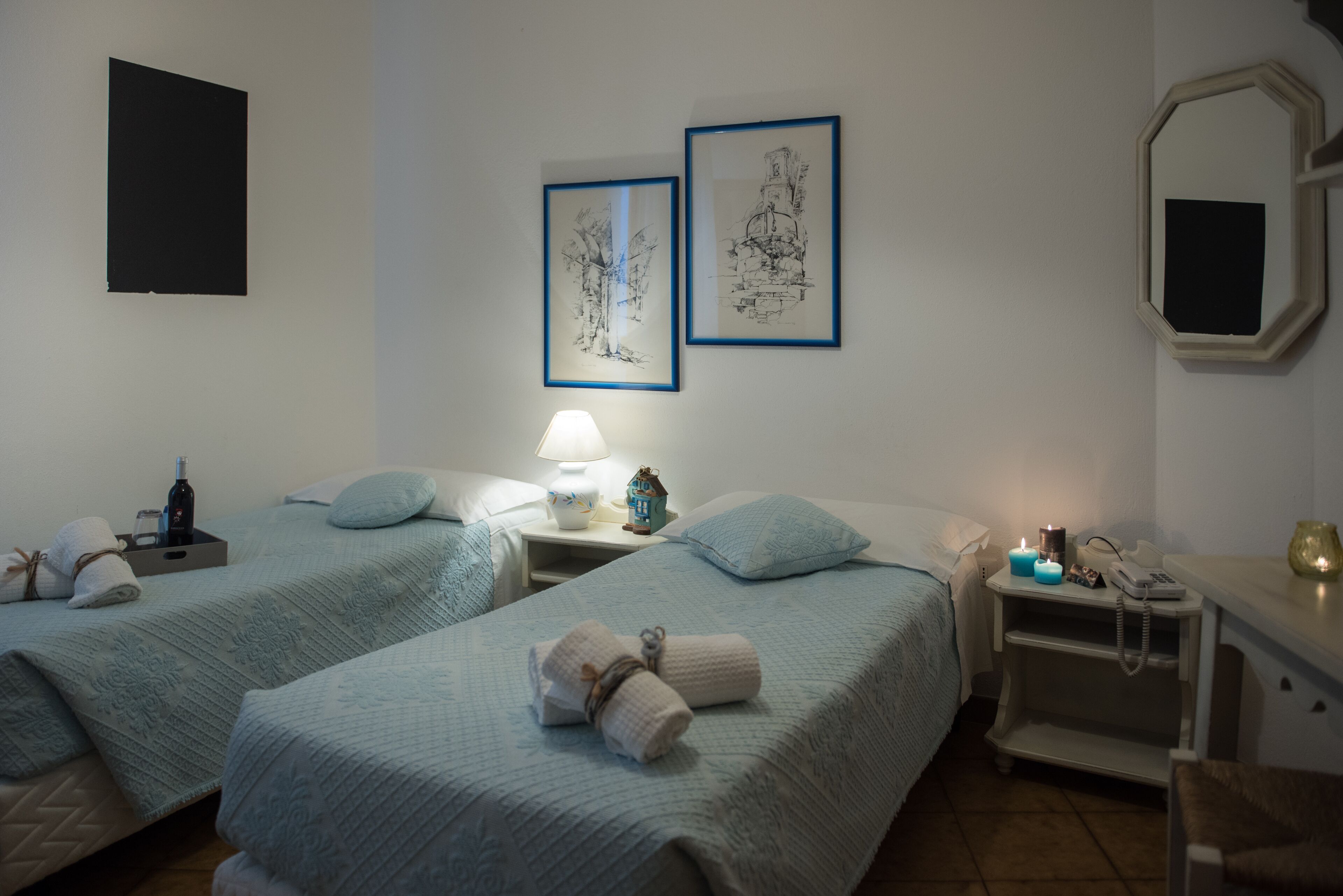 A hotel room with two beds, a nightstand with a lamp, a mirror, and framed artwork on the wall.