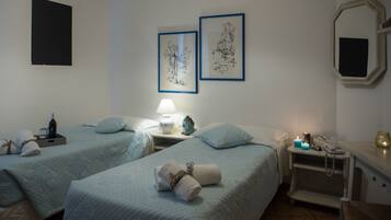 A hotel room with two beds, a nightstand with a lamp, a mirror, and framed artwork on the wall.