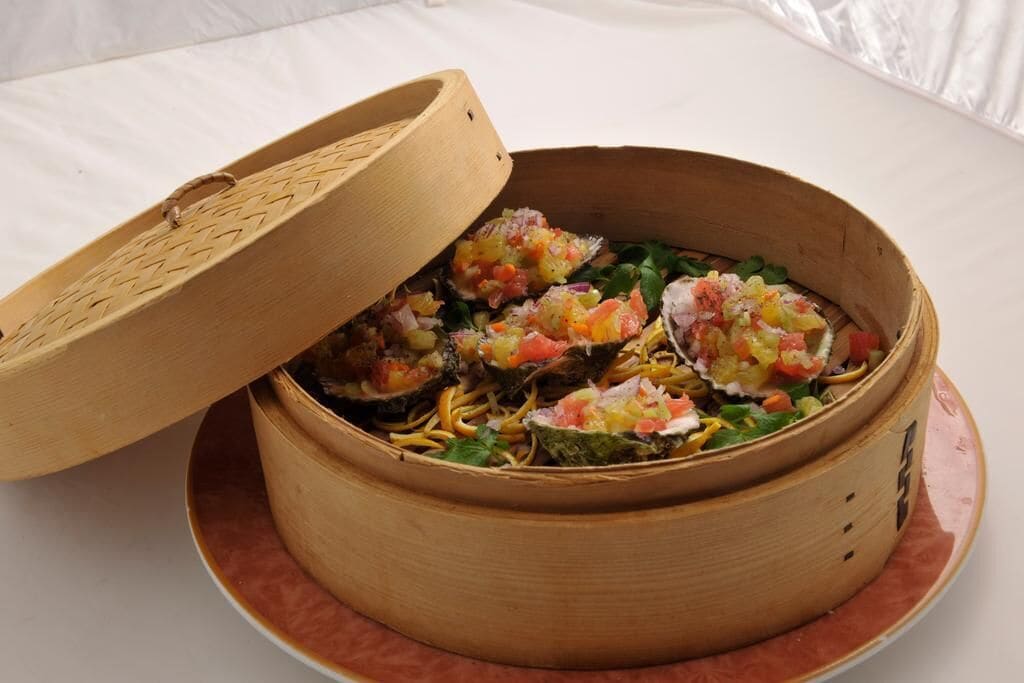 A bamboo steamer containing a colorful vegetable and noodle dish.