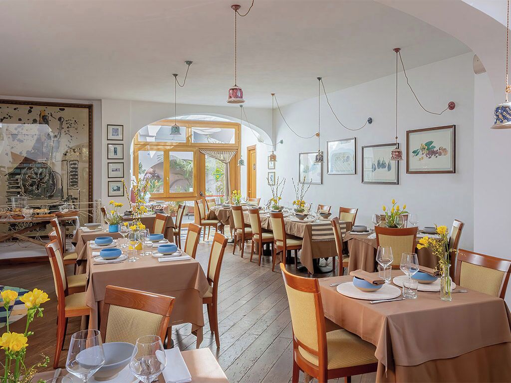 A dining area with multiple tables set for meals, wooden chairs, and hanging pendant lights.