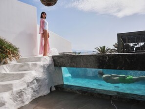 A pool with a clear view of the sea, a person swimming, and a person standing on a white staircase. - O by Myconian, Mykonos, a Member of Design Hotels (Mykonos)