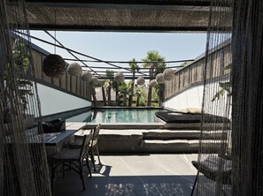 A pool area with a thatched roof, wicker furniture, and a view of palm trees. - O by Myconian, Mykonos, a Member of Design Hotels (Mykonos)