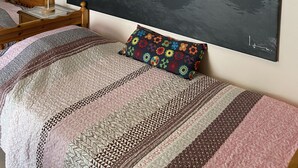 Een slaapkamer met een bed, een nachtkastje met een lamp en een groot schilderij van een rotsachtige kustlijn.