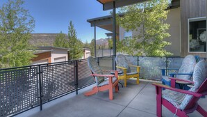Un balcon abrité, agrémenté de chaises aux couleurs vives, offrant une vue sur les arbres et les montagnes, et un bâtiment au design moderne.