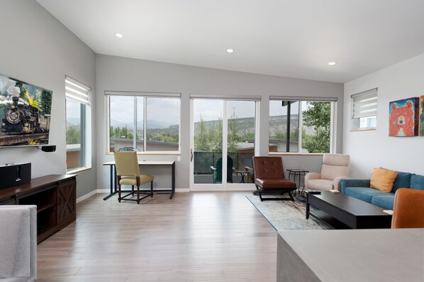 A spacious living room with a large sliding glass door leading to a balcony, a flat-screen TV mounted on the wall, and a cozy seating area with a sofa and chairs. - Townhome with Awesome Views - 1 Mile to Downtown - 30+ Day Stay Required (Durango)