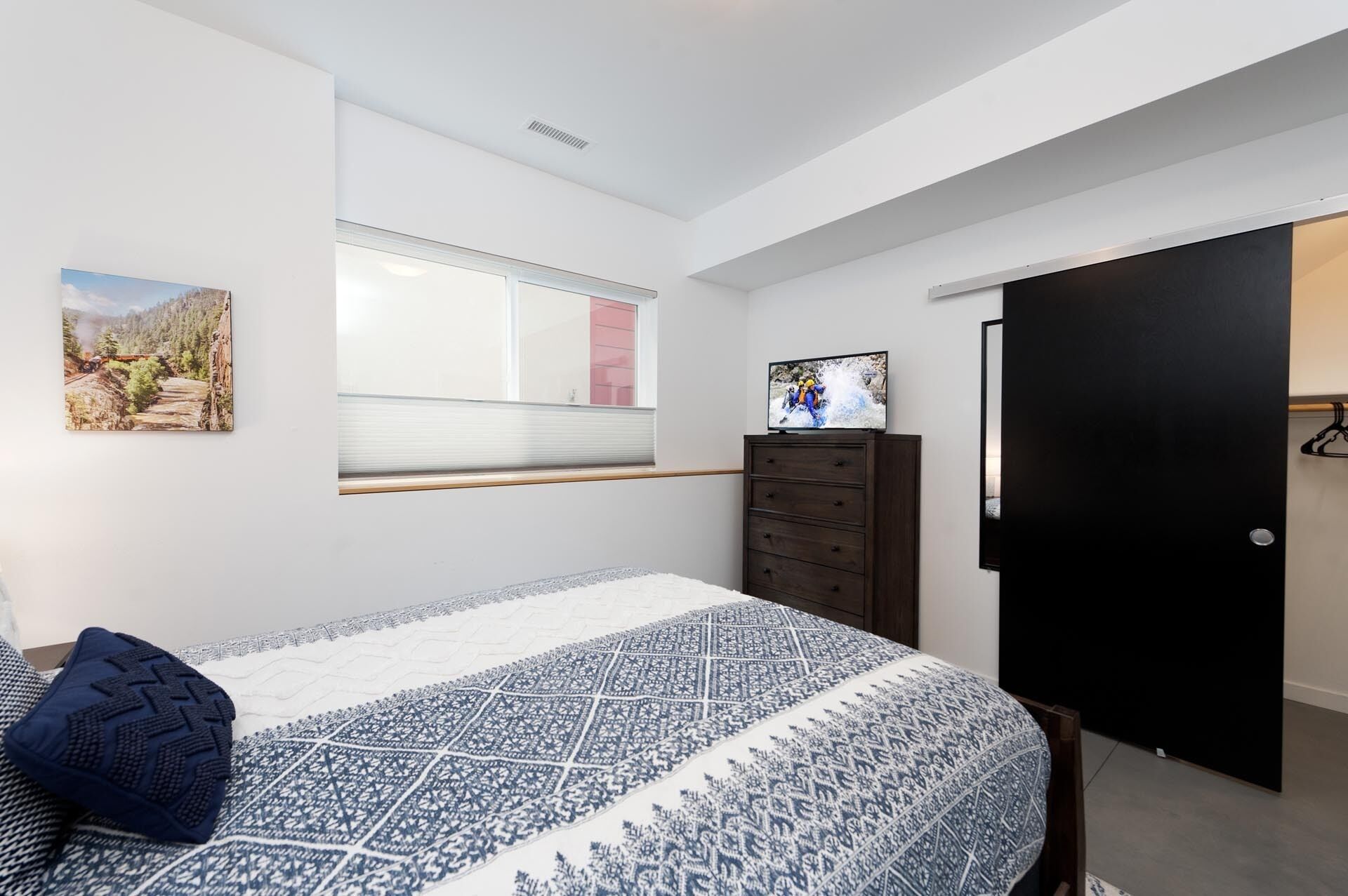 A bedroom with a bed, a dresser, a window, and a door.