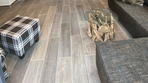 Een moderne woonkamer met een flatscreen televisie aan een wand, een glazen salontafel en een bank met kussens.