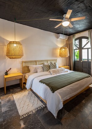 Ein Schlafzimmer mit einem Bett, zwei Nachttischen, einem Deckenventilator und einem großen Fenster mit Vorhängen.