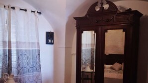 Un dormitorio con una cama, un armario, una araña y una ventana con cortinas.