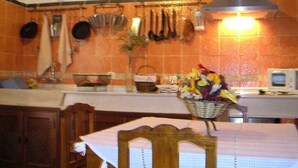 Una cocina con baldosas naranjas, ollas colgantes, un microondas y una mesa con una cesta de fruta.