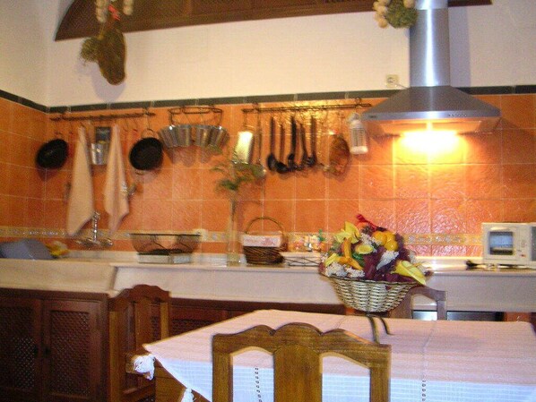 A kitchen with orange tiles, hanging pots, a microwave, and a table with a basket of fruit.