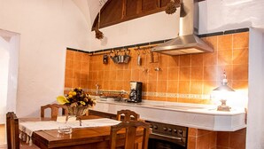 Una cocina con una mesa de madera, sillas, estufa y cafetera.