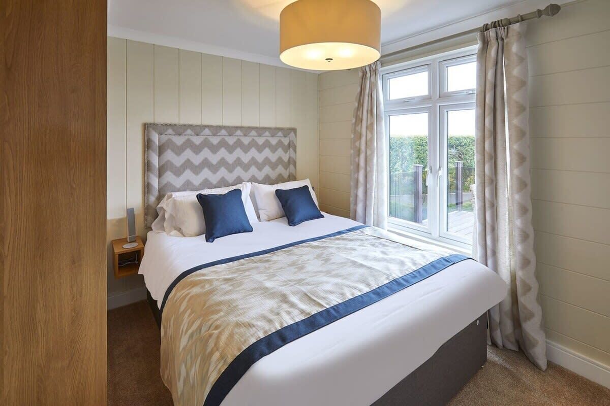 Une chambre à coucher avec un lit, une table de chevet, une fenêtre avec des rideaux et une vue sur la verdure à l’extérieur.