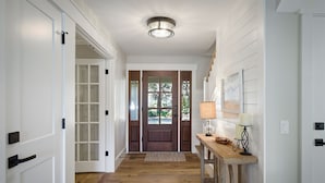 Un couloir avec des portes blanches, un plancher en bois, une porte en bois sombre au fond, et une table avec deux lampes.