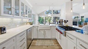 Une cuisine moderne avec des meubles blancs, un îlot central et une grande fenêtre qui laisse entrer la lumière naturelle.