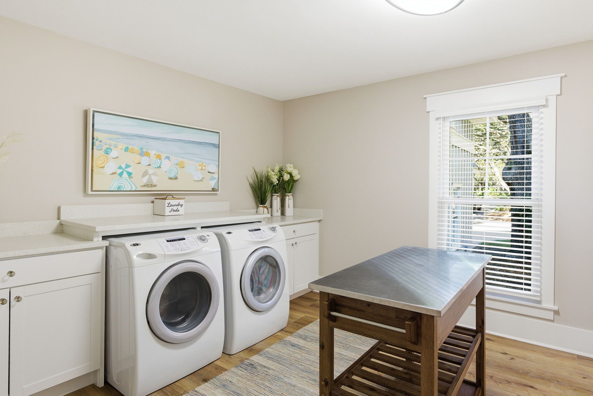 A laundry room with two washing machines, a table, and a window with blinds.