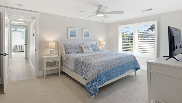 A bedroom with a bed, nightstands, a ceiling fan, a TV, and a window with blinds.