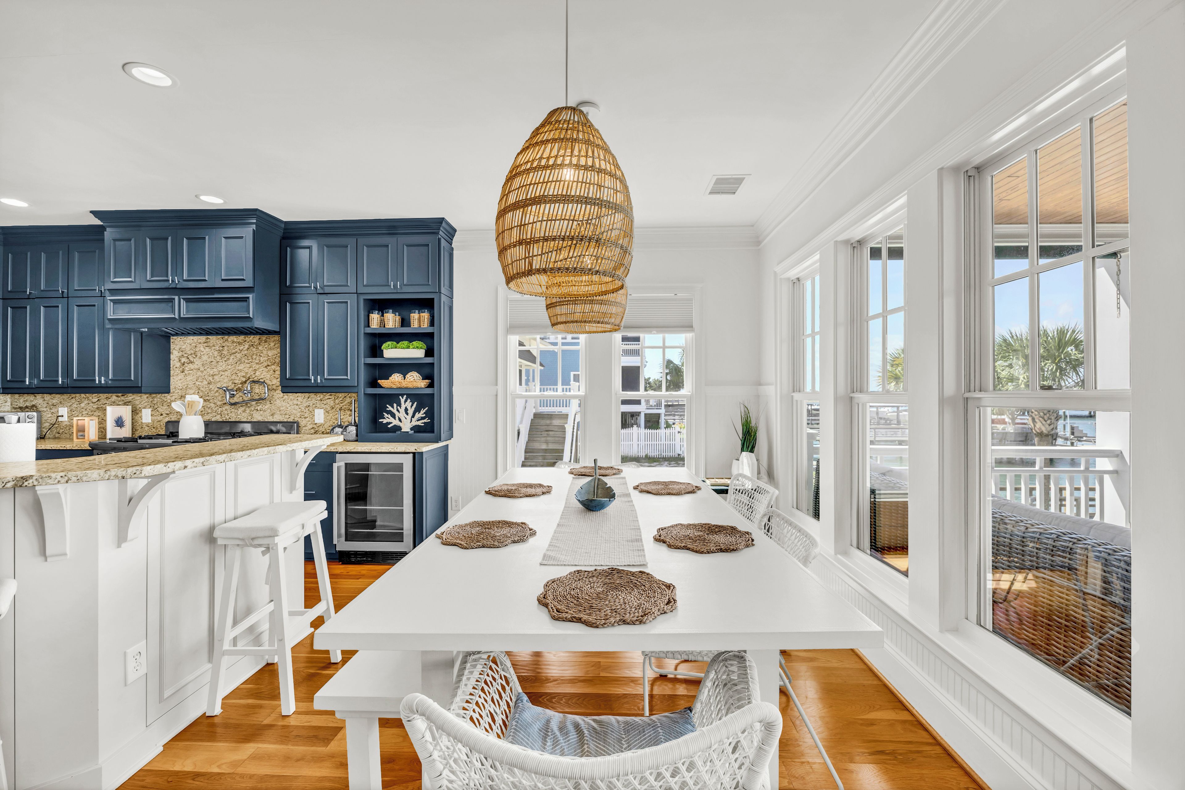 A modern kitchen with dark blue cabinets, a white island, and a large dining table with woven placemats.