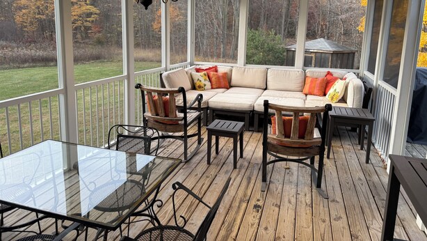 Un porche cubierto con una mesa de vidrio, sillas, un sofá y una araña.