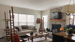 Una sala de estar con sofá, mesa de centro y sillones. Hay una chimenea con un televisor encima.
