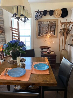 A dining area with a wooden table, two blue plates, a candle, and a vase of blue flowers. - A River Runs Through It-10 private acres on the Black River, South Haven (Pullman)
