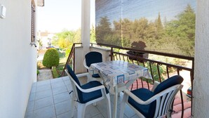 Un balcon avec une table et des chaises, un moustiquaire et une vue sur la verdure et les bâtiments.
