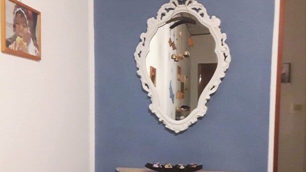 Una stanza con una parete blu, uno specchio bianco decorato e un consolle bianco con basamento ornamentale.