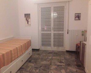 Ein Schlafzimmer mit Bett, Kleiderschrank, einer Tür mit einem Glasspiegel und einem Heizkörper.