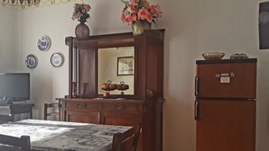 Zona pranzo con tavolo e sedie in legno, uno specchio sopra il tavolo e un frigorifero alla destra.