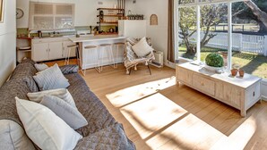 Cocina moderna con armarios blancos, un taburete de bar y vistas al jardín trasero a través de grandes ventanales.