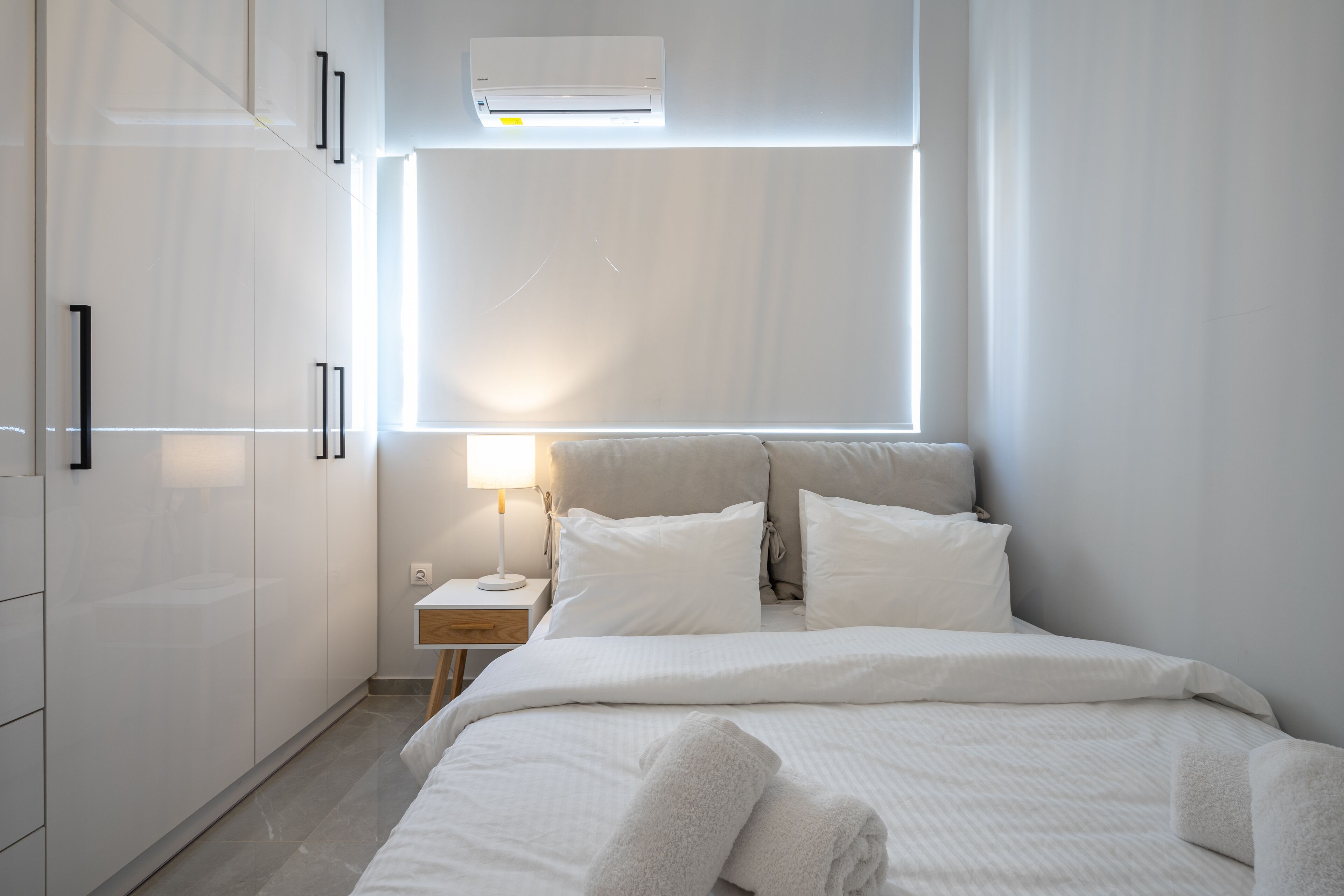 A modern bedroom with a bed, bedside table, lamp, and an air conditioning unit.