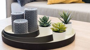 Ein modernes Wohnzimmer mit einem grauen Sofa, einem gelben Kissen sowie einer Ablage mit Kerzen und kleinen Topfpflanzen.