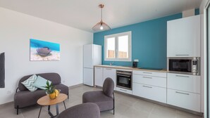 A modern kitchen with white cabinets, a microwave, and a stove. There is a dining area with a sofa and chairs, and a painting of a stingray on the wall.