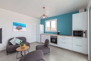 A modern kitchen with white cabinets, a microwave, and a stove. There is a dining area with a sofa and chairs, and a painting of a stingray on the wall.