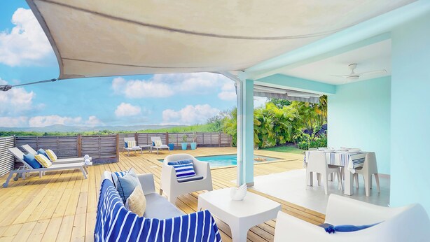 A covered outdoor deck with lounge chairs, a pool, and a dining area.