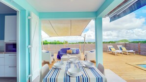 A covered outdoor dining area with a table set for four, a sofa, and a poolside lounge area.