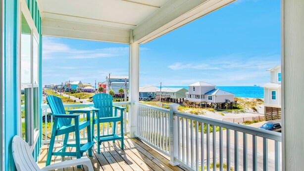 A wooden deck with chairs and a table, overlooking a beach and houses. - Luxury Coastal Retreat | Gulf Views | Private Elevator (Gulf Shores)